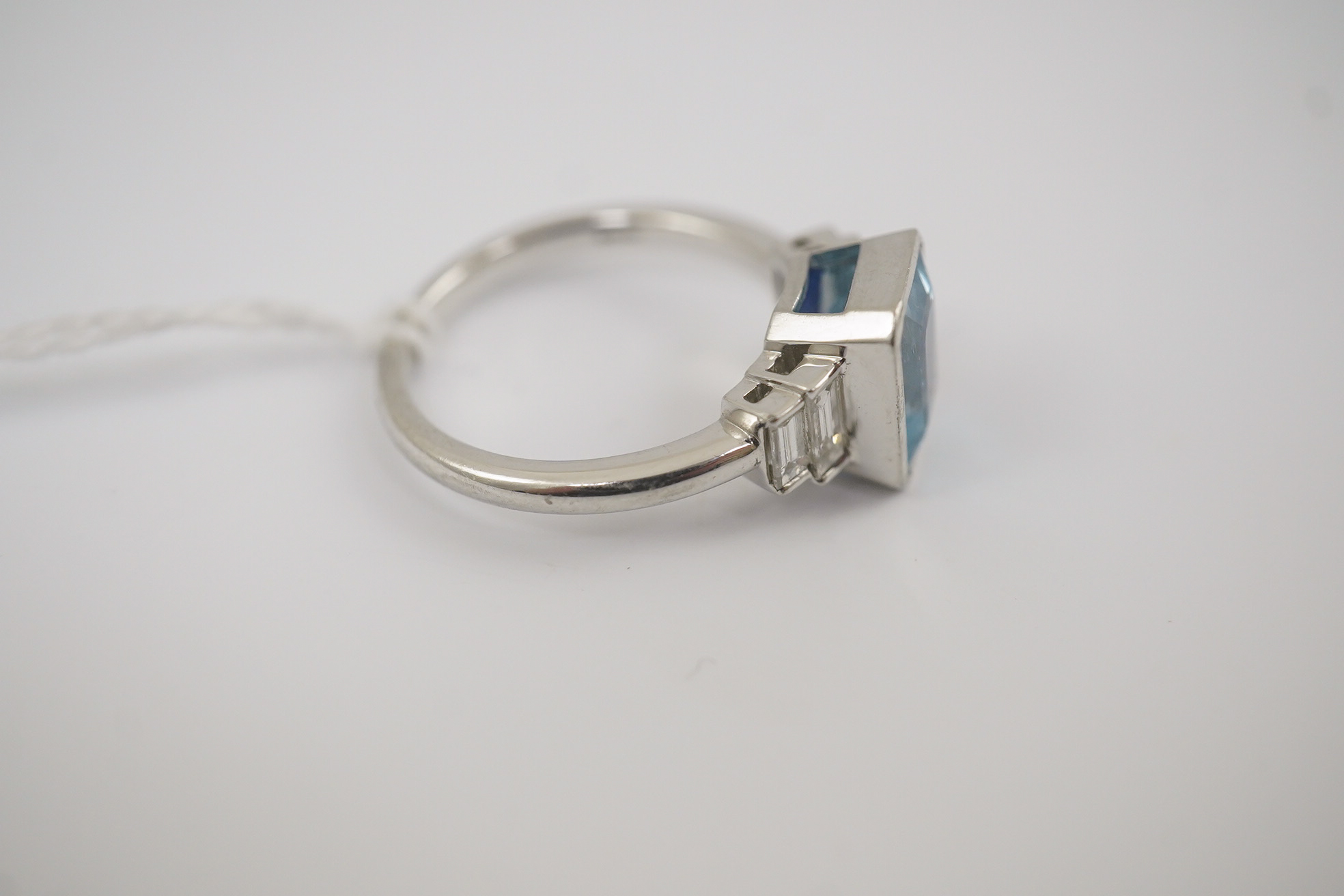 An Art Deco style platinum and single stone emerald cut aquamarine set dress ring, with four stone graduated baguette cut diamond set shoulders